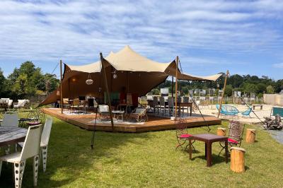 Espace lumineux avec mobilier en bois et cuir, grandes fenêtres, plafond en poutres apparentes et sol en béton.