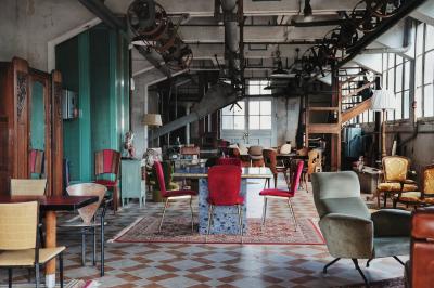 Espace lumineux avec mobilier en bois et cuir, grandes fenêtres, plafond en poutres apparentes et sol en béton.