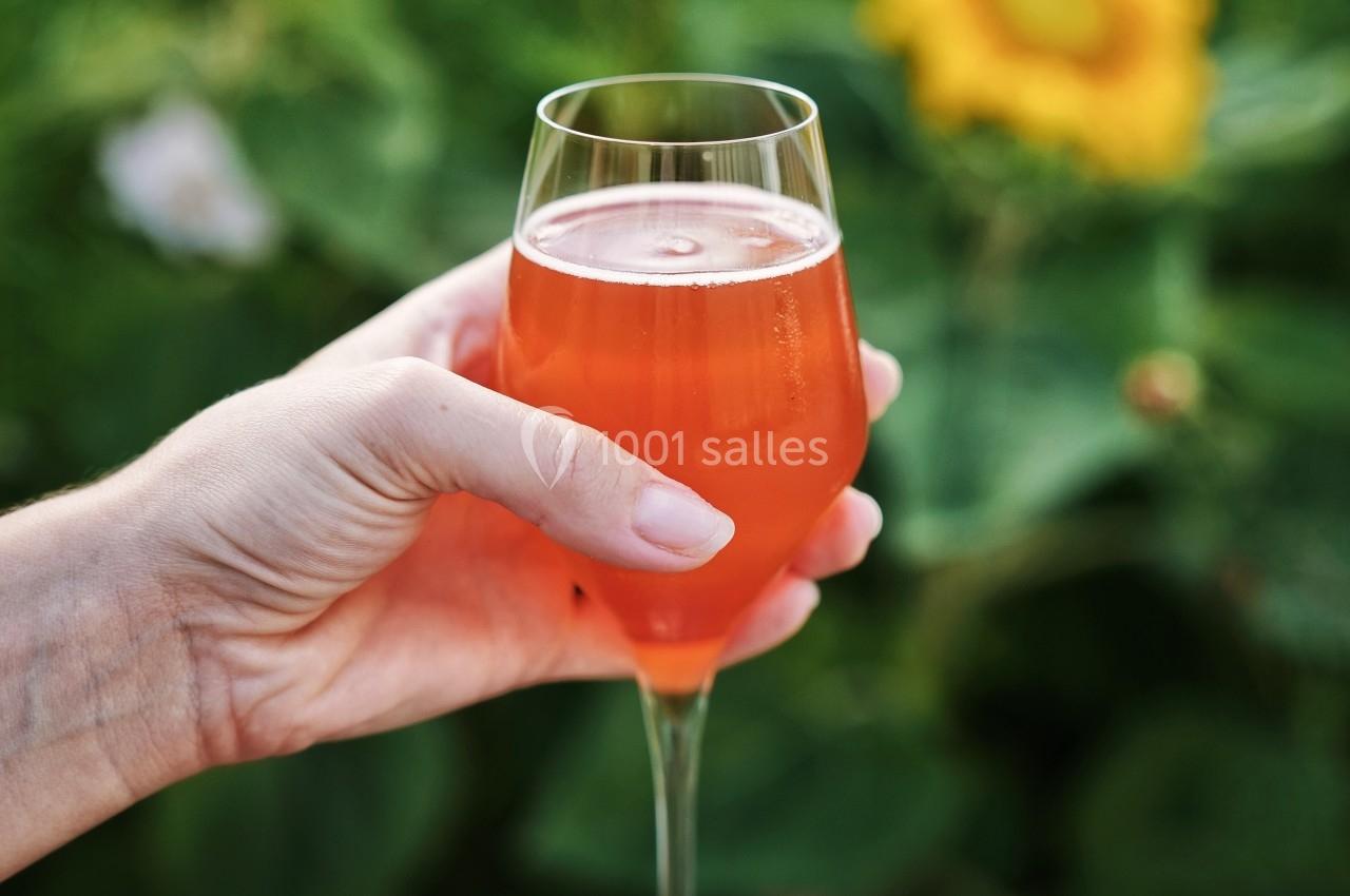 Main tenant un verre de boisson orange pétillante devant un fond de tournesols et de verdure.