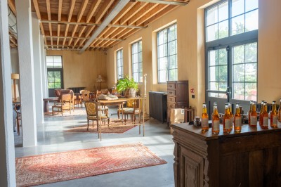 Espace lumineux avec mobilier en bois et cuir, grandes fenêtres, plafond en poutres apparentes et sol en béton.