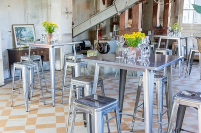 Espace lumineux avec mobilier en bois et cuir, grandes fenêtres, plafond en poutres apparentes et sol en béton.