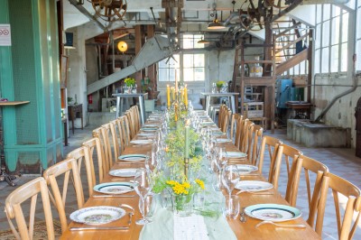 Espace lumineux avec mobilier en bois et cuir, grandes fenêtres, plafond en poutres apparentes et sol en béton.