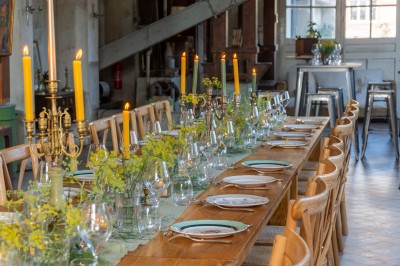 Espace lumineux avec mobilier en bois et cuir, grandes fenêtres, plafond en poutres apparentes et sol en béton.