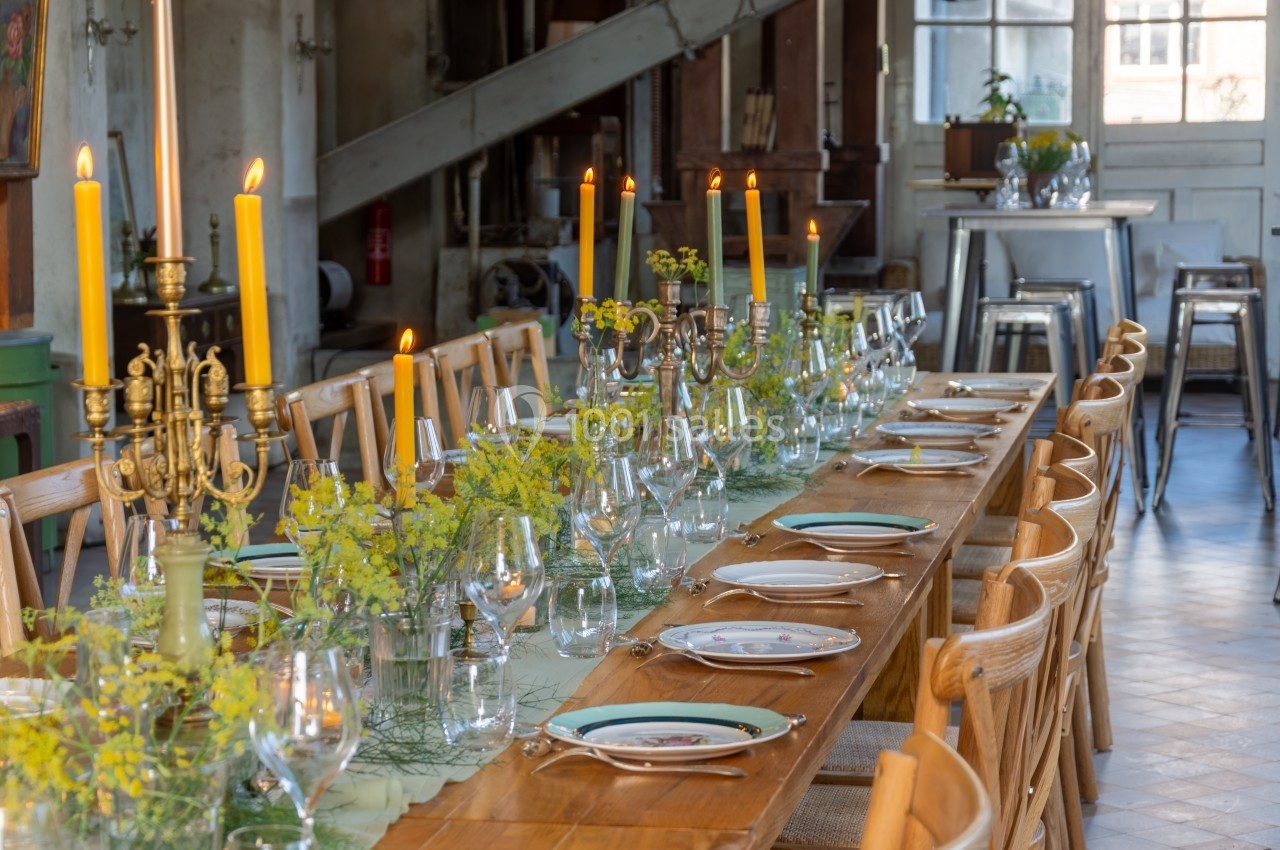 Table en bois dressée avec chandeliers, bougies allumées, vaisselle élégante et décorations florales jaunes.