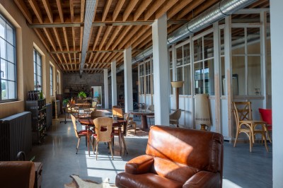 Espace lumineux avec mobilier en bois et cuir, grandes fenêtres, plafond en poutres apparentes et sol en béton.