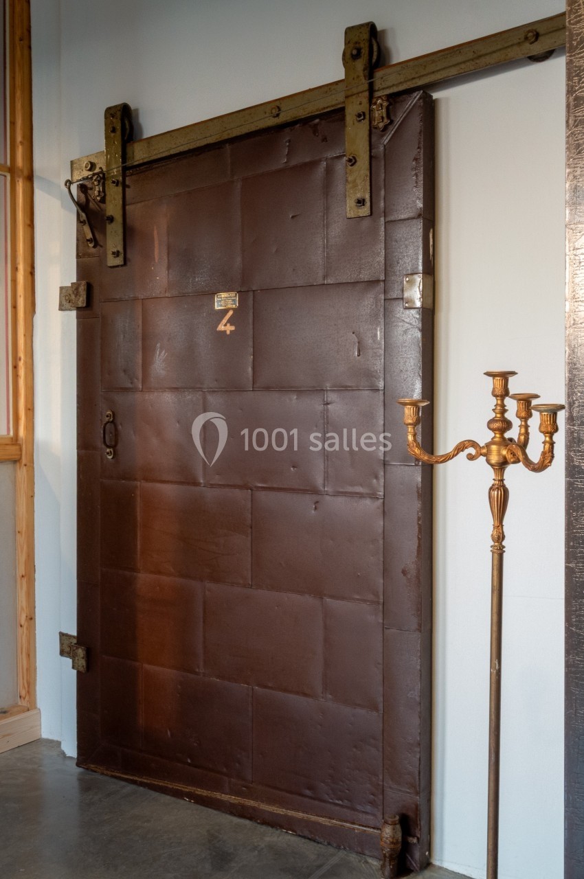 Porte coulissante en métal brun avec un mécanisme visible, située dans un intérieur au style industriel.