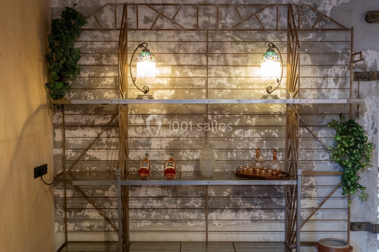 Étagère métallique décorative avec quelques bouteilles, un plateau et des plantes, éclairée par deux lampes murales.