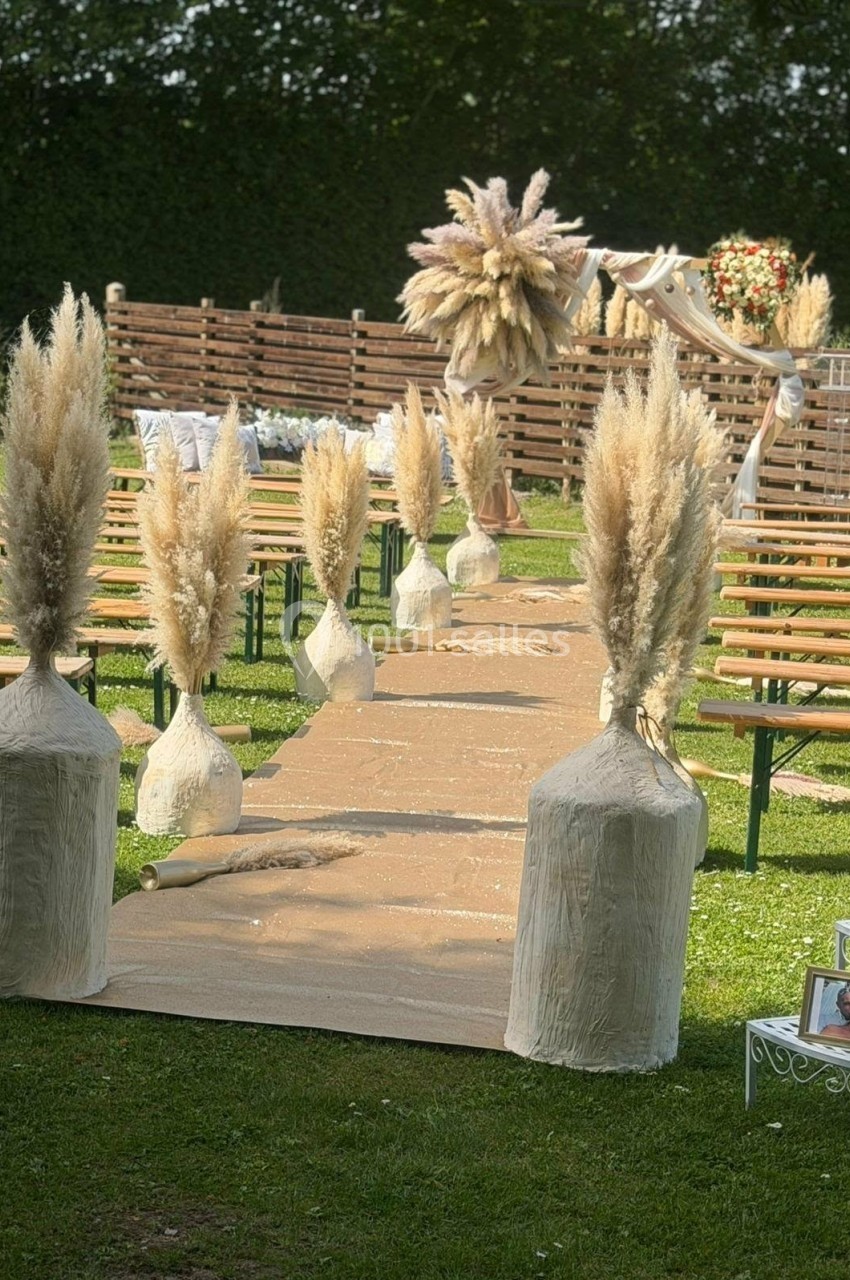 Allée extérieure décorée de bottes d'herbes de la pampa, menant à une arche florale pour une cérémonie en plein air.