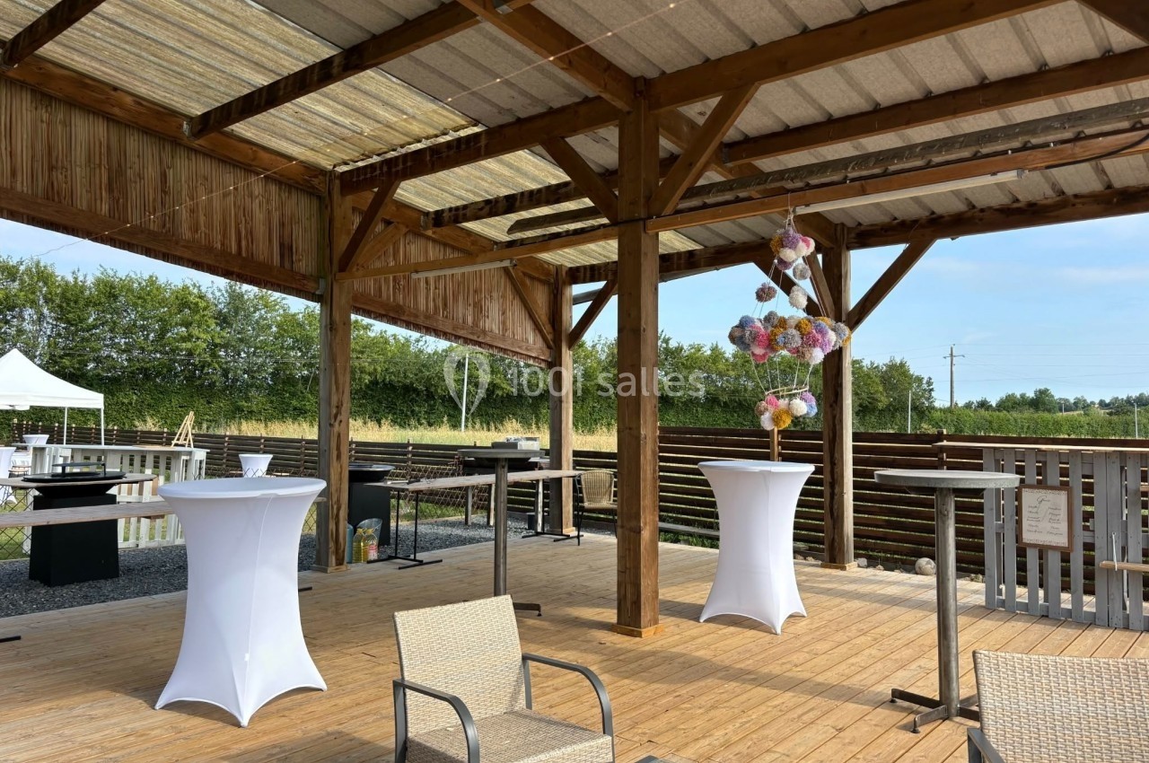 Terrasse en bois couverte avec des tables hautes décorées, des chaises et un espace aménagé en extérieur.