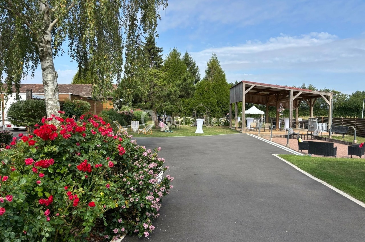 Allée bordée de fleurs colorées menant à une pergola en bois dans un espace extérieur arboré.