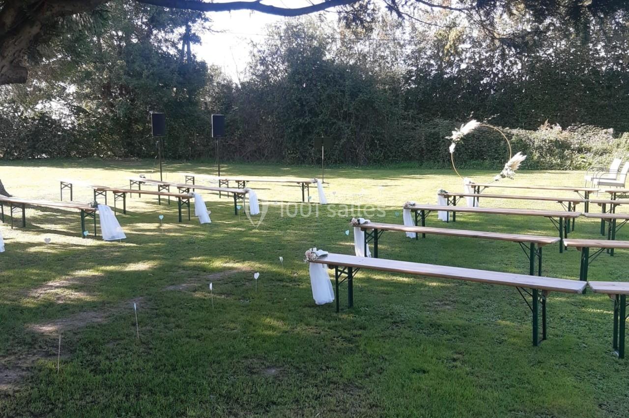 Chaises et bancs disposés en extérieur sous un arbre, avec une arche décorative en arrière-plan pour une cérémonie.
