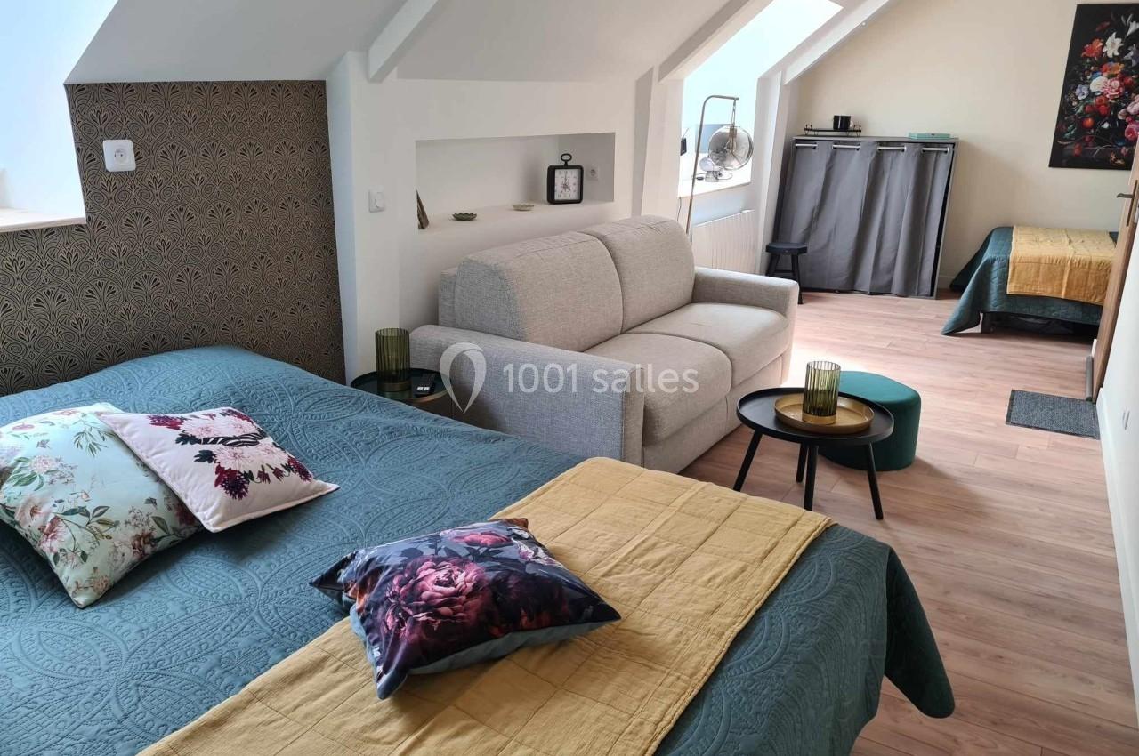 Chambre mansardée avec lit double, canapé, table basse, lit simple en arrière-plan et décoration florale.