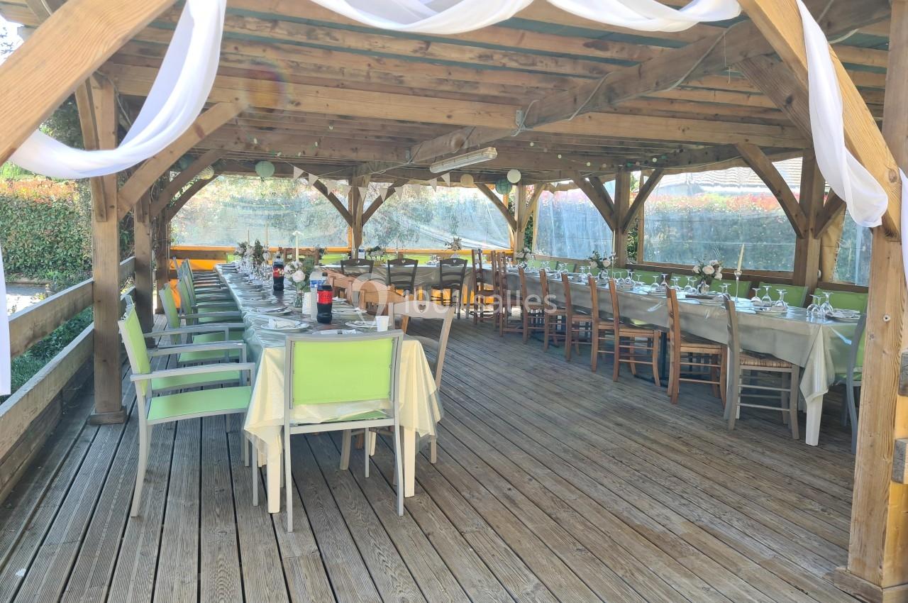 Tables dressées sous une pergola en bois, décorée de voilages blancs, pour un repas ou un événement en extérieur.