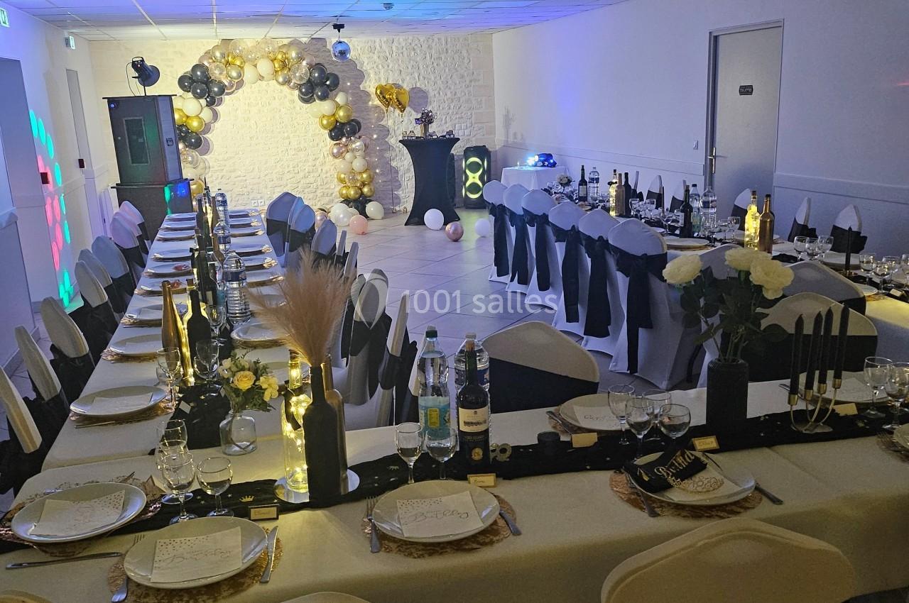 Salle décorée pour une fête d'anniversaire avec tables dressées, ballons dorés et noirs, et arche lumineuse.