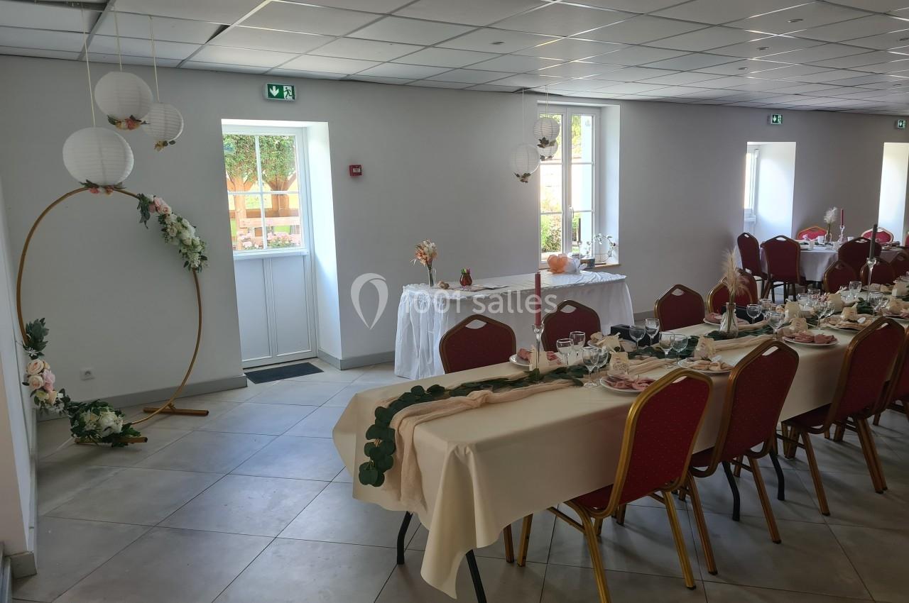 Salle de réception décorée pour un événement, avec tables dressées, chaises rouges et ornements floraux.