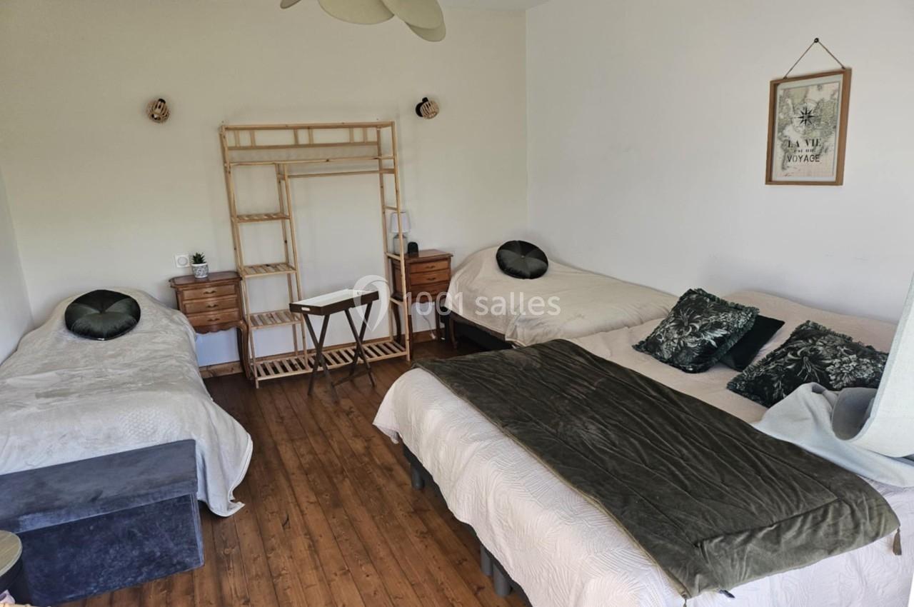 Chambre lumineuse avec trois lits simples, parquet en bois, mobilier minimaliste et décoration sobre.