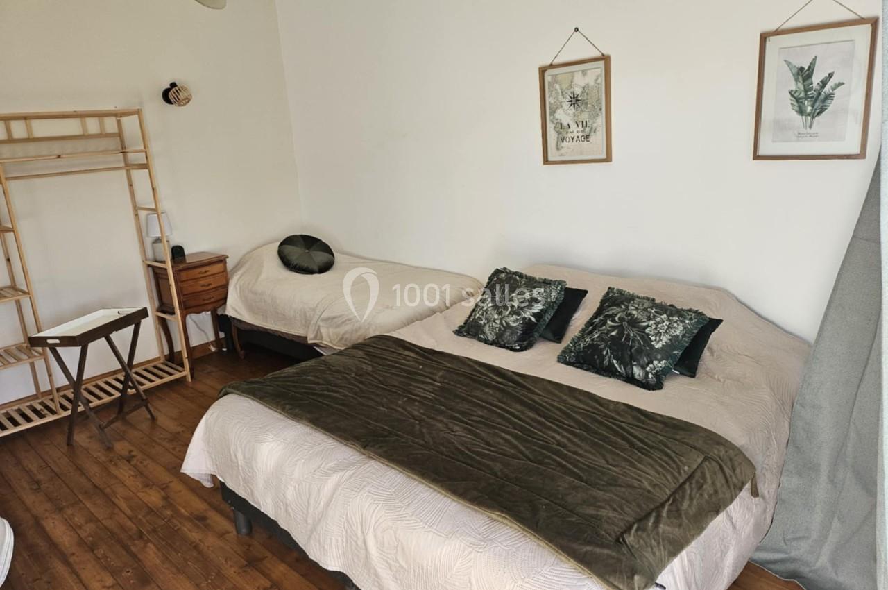 Chambre avec un lit double, un lit simple, des coussins verts, un portant en bois et des cadres décoratifs au mur.