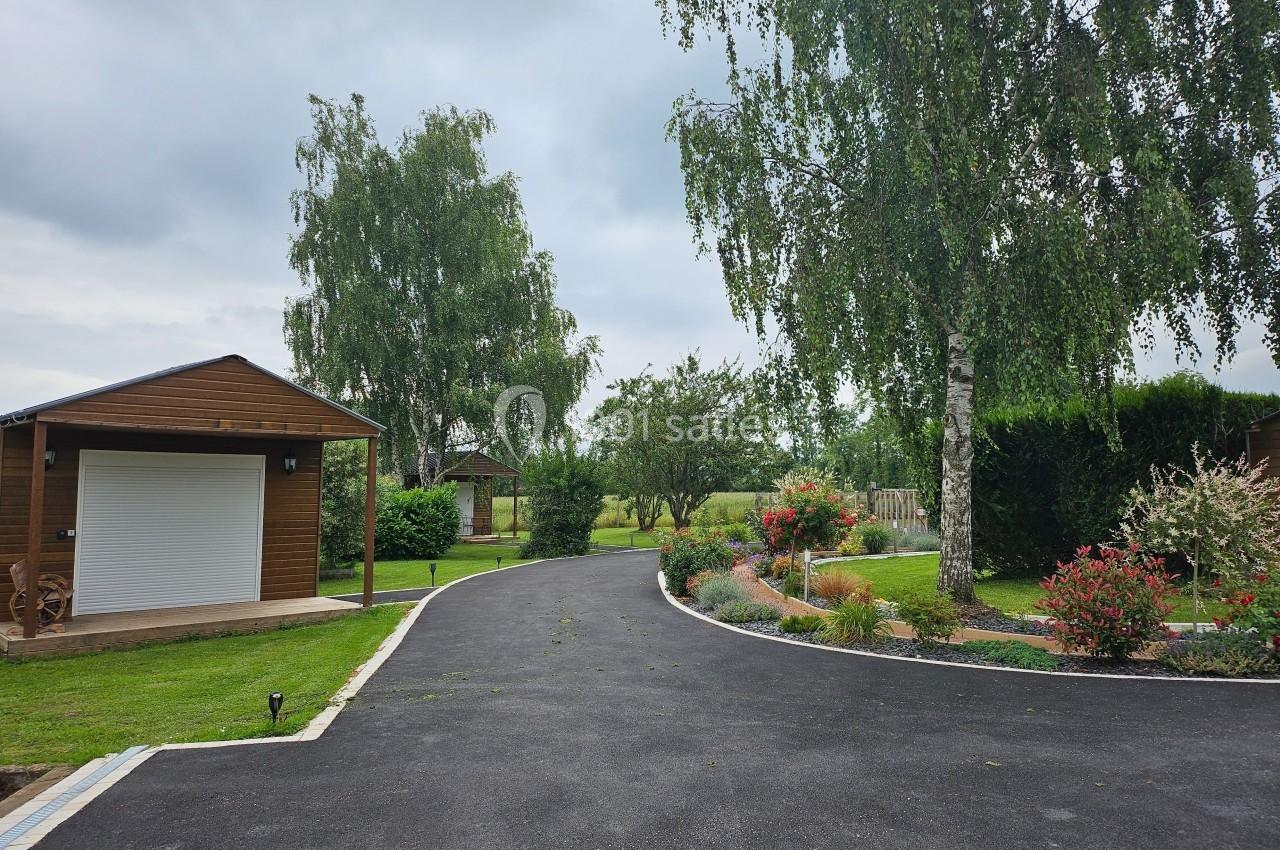 Allée asphaltée bordée de pelouses, d'arbres et de buissons fleuris, avec des cabanons en bois en arrière-plan.