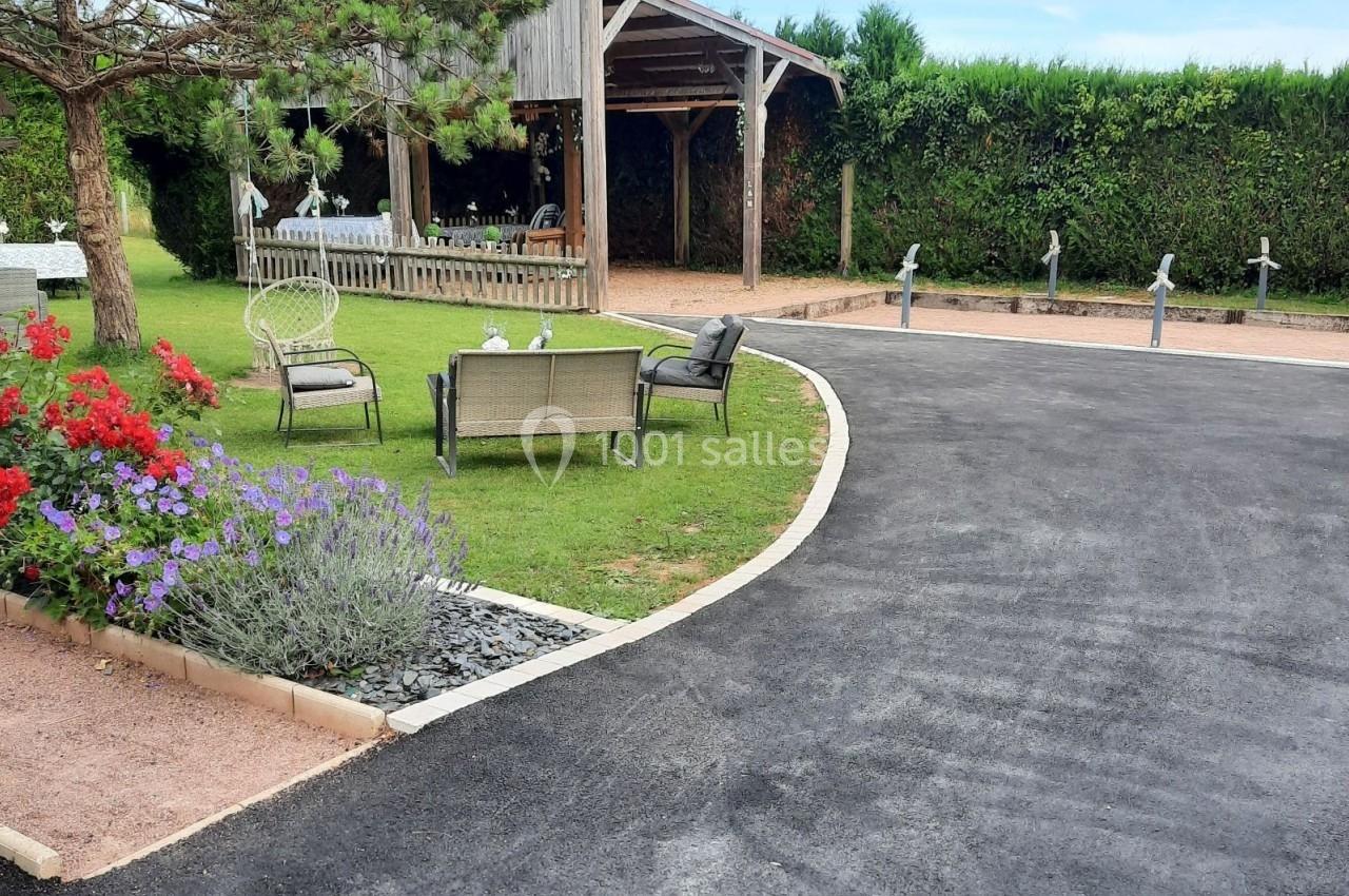 Allée asphaltée menant à un jardin avec pelouse, fleurs, mobilier d'extérieur et une pergola en bois.