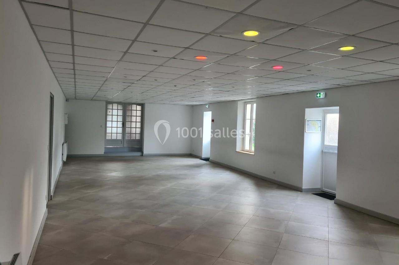 Salle vide avec carrelage clair, plafond à dalles blanches et quelques lumières colorées allumées.