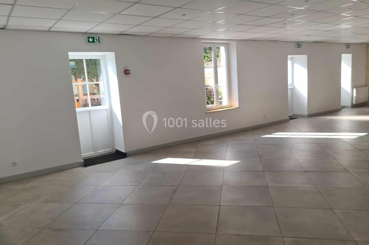 Salle lumineuse avec carrelage clair, murs blancs, fenêtres et portes donnant sur l'extérieur.