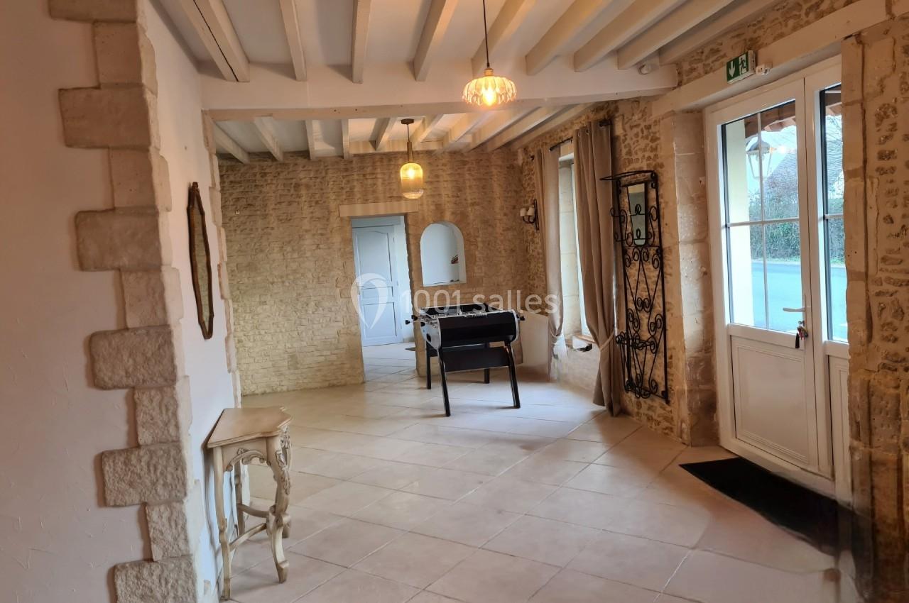 Salle lumineuse avec murs en pierre, table de baby-foot, meubles décoratifs et porte-fenêtre donnant sur l'extérieur.