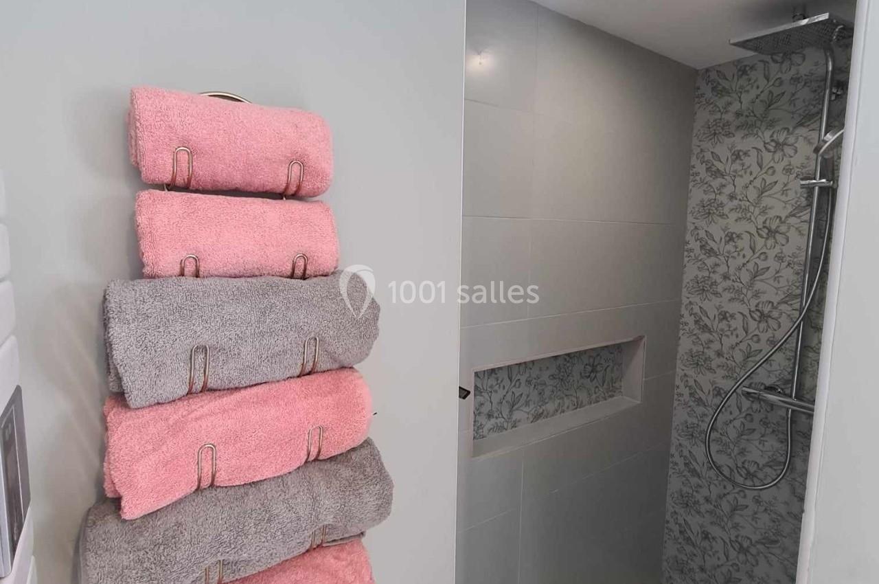 Salle de bain moderne avec douche à l'italienne, mur carrelé floral et serviettes pliées sur un porte-serviettes.