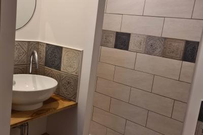 Douche à l'italienne avec carrelage sombre à gauche et lavabo blanc sur meuble en bois à droite.