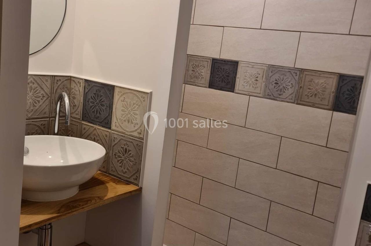 Salle de bain avec lavabo rond sur étagère en bois, miroir circulaire et douche avec carrelage beige et décoratif.