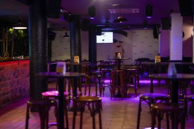 Salle de bar avec tables et chaises en bois, éclairage tamisé violet et écran au fond.