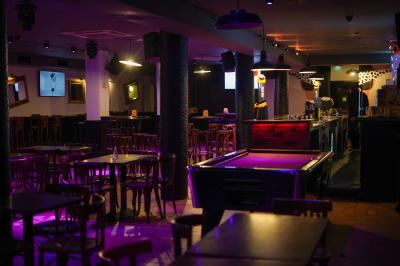 Salle de bar avec tables et chaises en bois, éclairage tamisé violet et écran au fond.