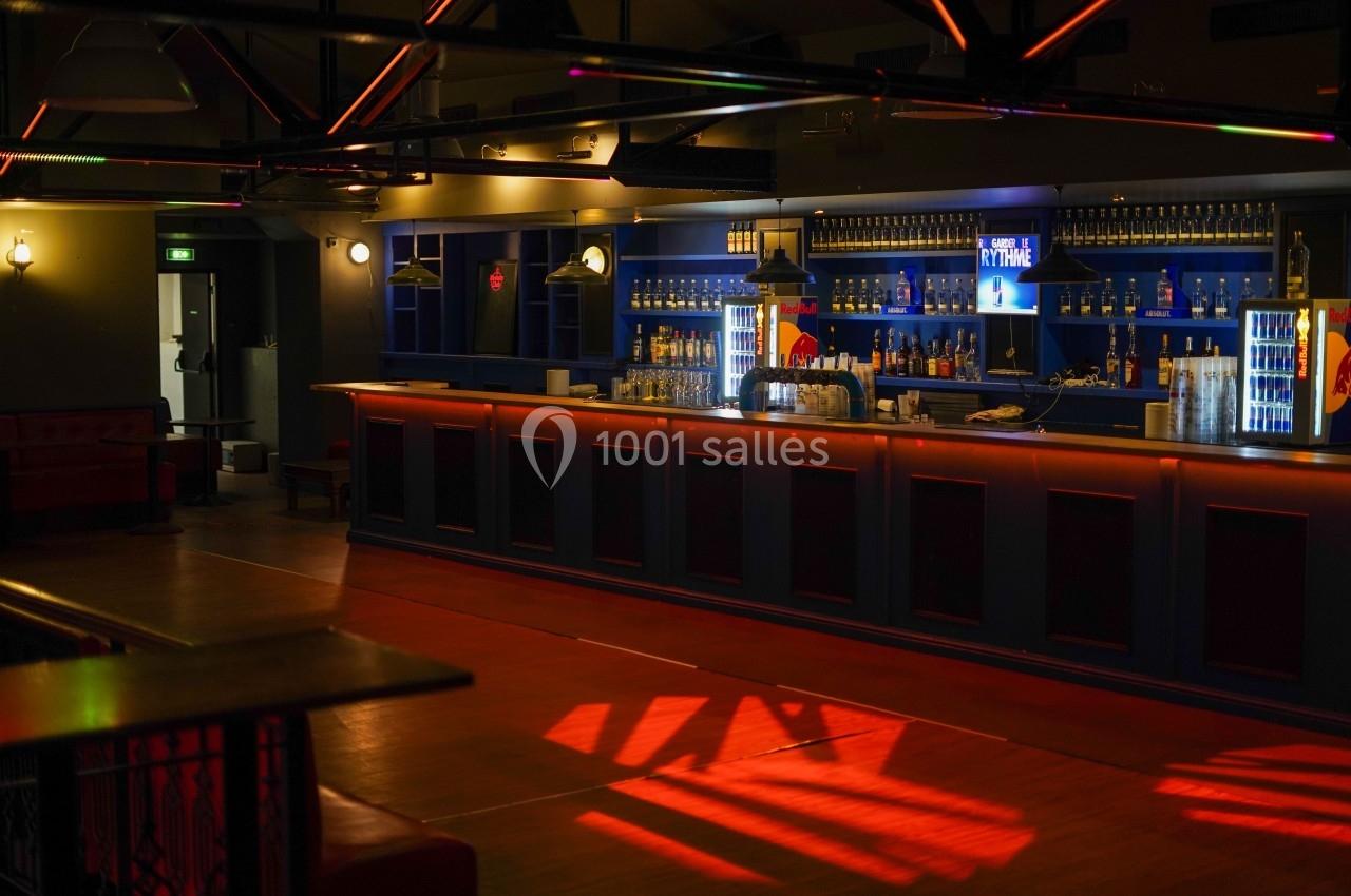 Bar moderne avec comptoir éclairé, étagères remplies de bouteilles, lumières tamisées et ambiance chaleureuse.