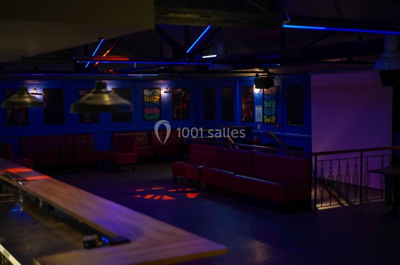 Salle de bar vide avec banquettes rouges, éclairage tamisé et néons colorés au plafond.