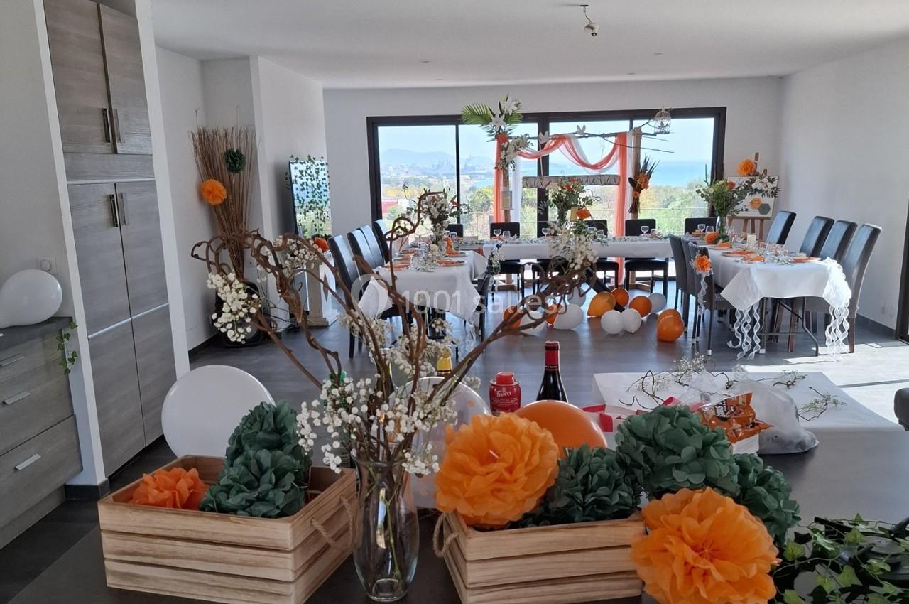 Salle décorée pour une réception avec des tables dressées, des fleurs, des ballons et une vue sur l'extérieur.