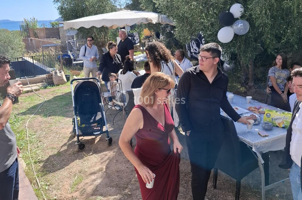 Des personnes discutent et partagent un moment convivial lors d'une fête en extérieur, avec des tables et des décorations.
