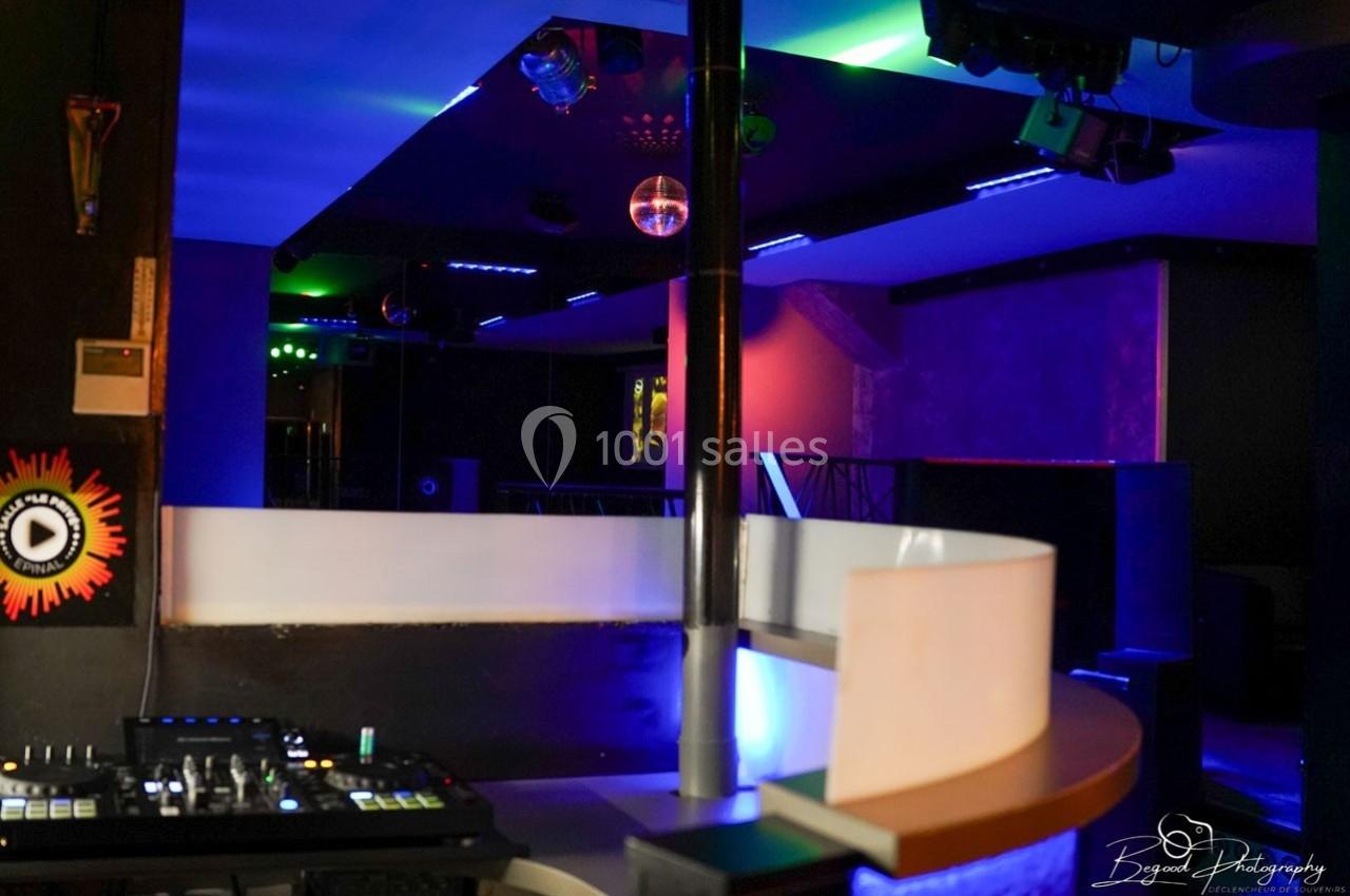 Intérieur d'une discothèque avec jeux de lumières colorées, une console de DJ et une piste de danse vide.