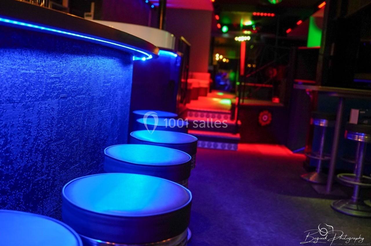 Tabourets alignés le long d'un bar éclairé par des lumières colorées dans un espace intérieur moderne et sombre.