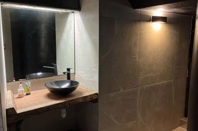 Vue d'une salle de bain avec un lavabo en vasque noire sur un plan en bois et un éclairage mural tamisé.
