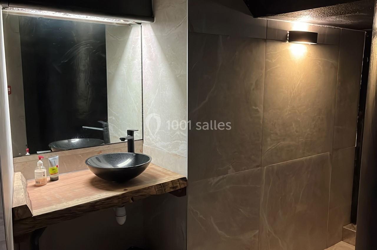 Vue d'une salle de bain avec un lavabo en vasque noire sur un plan en bois et un éclairage mural tamisé.