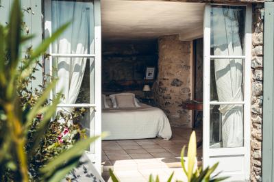 Chambre rustique avec lit double, poutres apparentes, mobilier en bois et salle de bain attenante en arrière-plan.