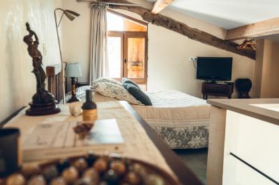 Chambre rustique avec lit double, poutres apparentes, mobilier en bois et salle de bain attenante en arrière-plan.