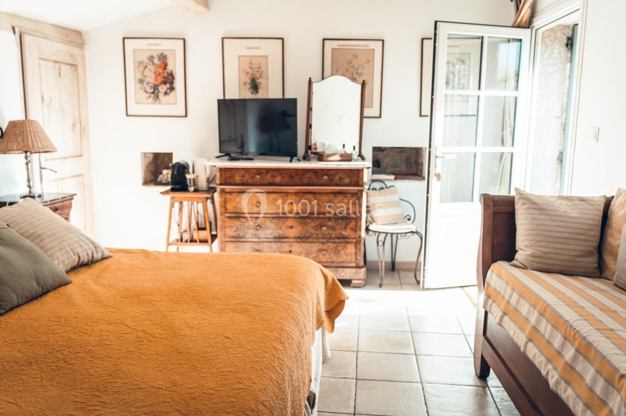 Chambre lumineuse avec lit double, lit simple, commode en bois, télévision et décorations murales florales.