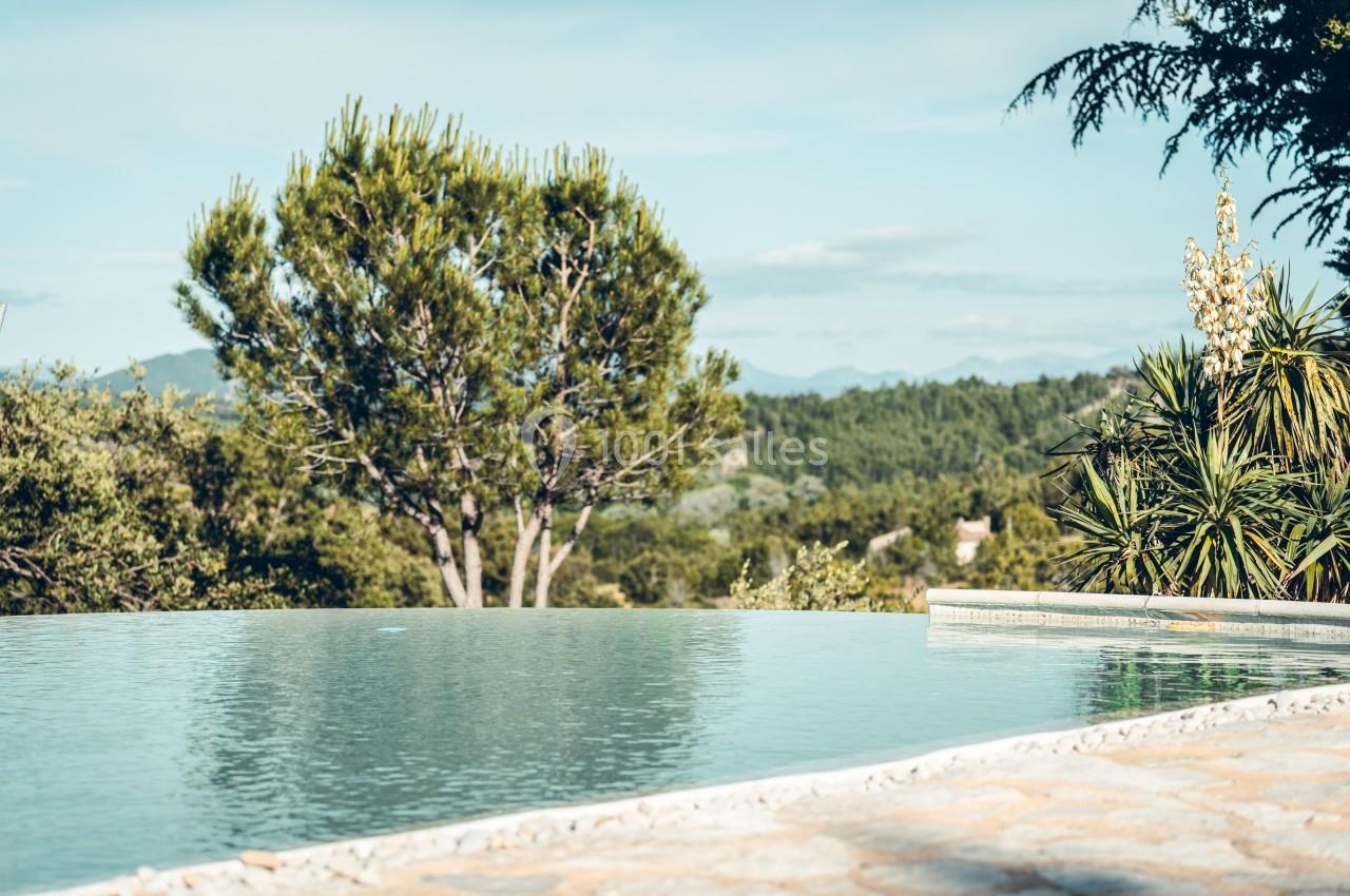 Piscine à débordement entourée de végétation avec vue sur une colline boisée sous un ciel dégagé.