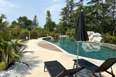 Piscine extérieure entourée de végétation, transats et parasols noirs, avec des rochers décoratifs au premier plan.