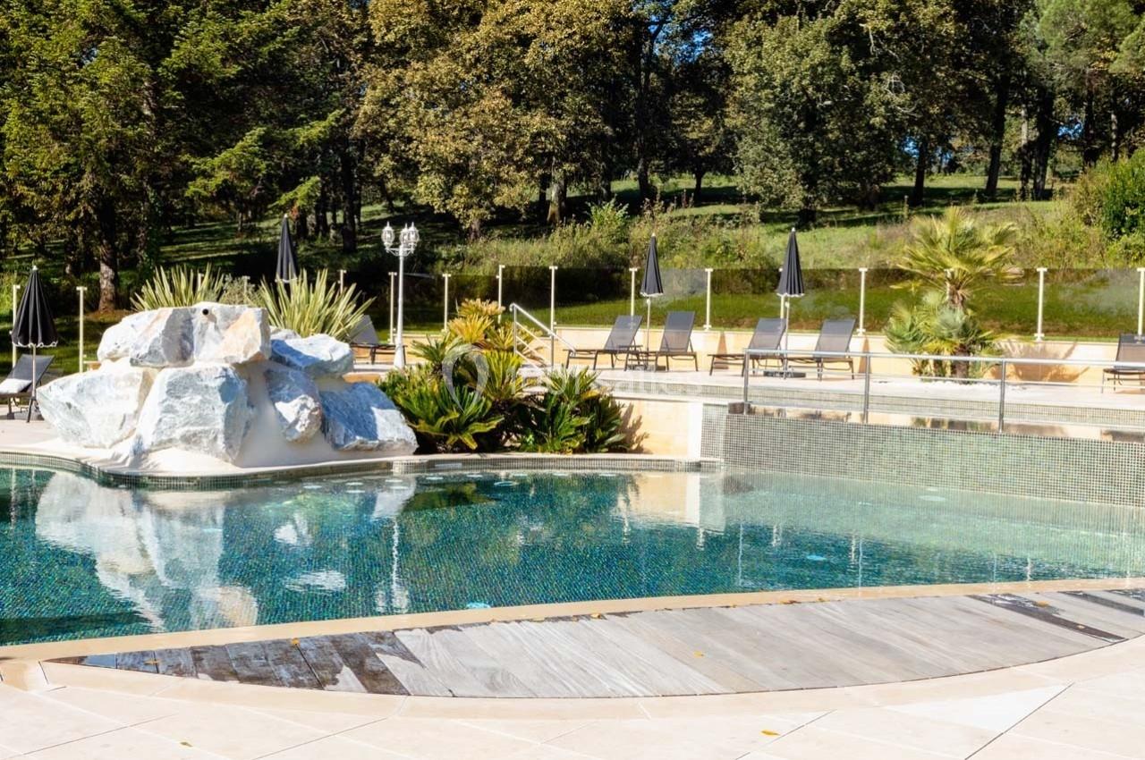 Piscine extérieure entourée de végétation, transats et parasols noirs, avec des rochers décoratifs au premier plan.