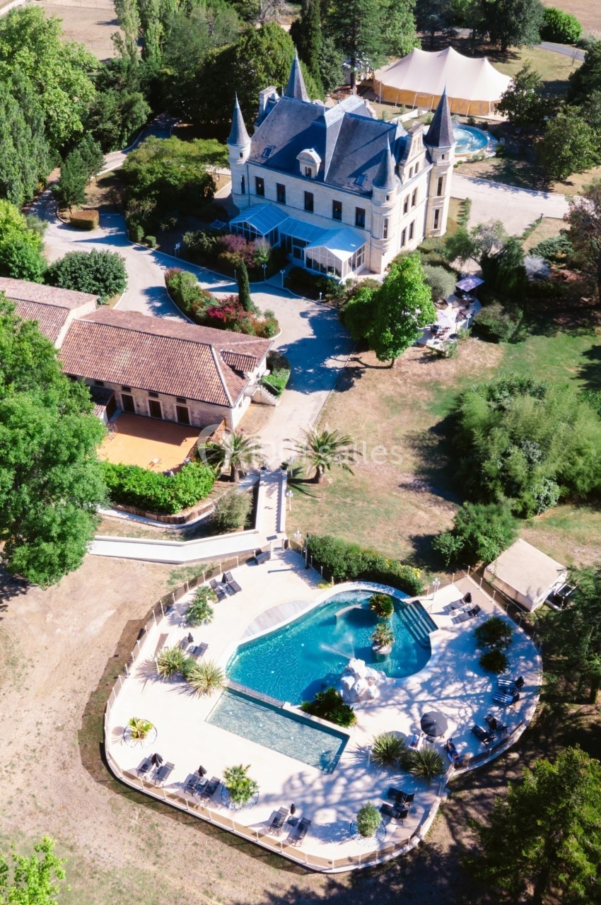 Vue aérienne d'un château entouré de jardins, avec une piscine en forme libre et des chaises longues à proximité.