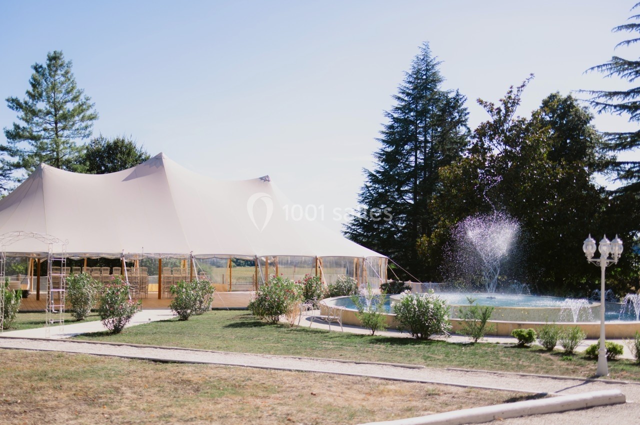 Tente beige installée près d'une fontaine entourée de verdure, dans un espace extérieur par temps clair.