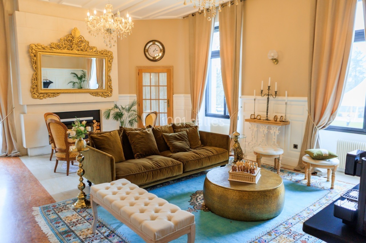 Salon élégant avec canapé en velours, miroir doré, lustres, table basse ronde et décoration raffinée.