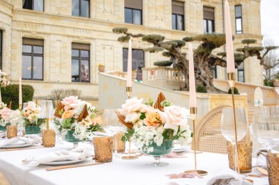 Table élégamment dressée en extérieur avec des fleurs pastel, des bougies et une grande bâtisse en arrière-plan.