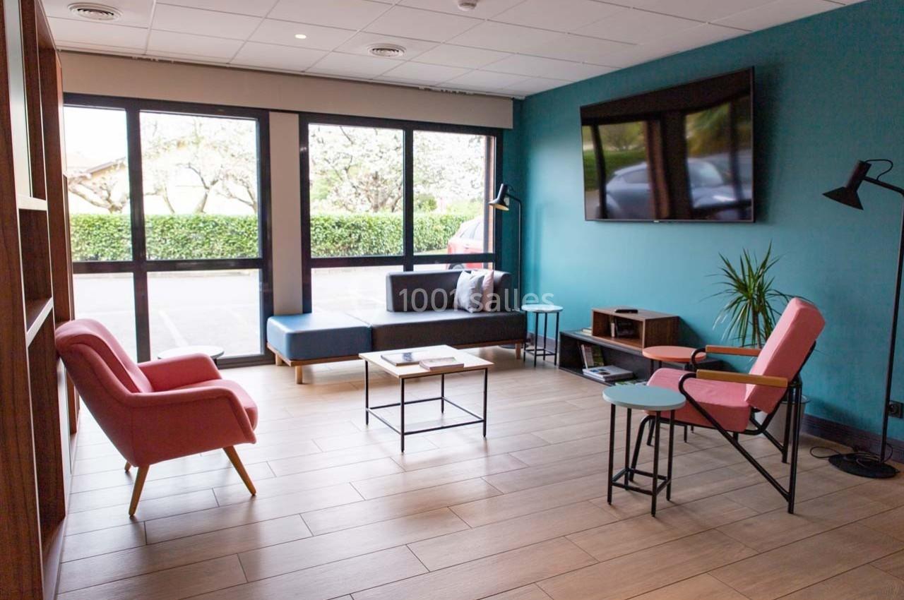 Salle d'attente lumineuse avec fauteuils, canapé, table basse et grande baie vitrée donnant sur un espace extérieur.